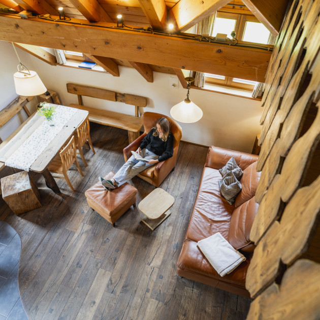 Ein Blick von der Galerie der Backhaus-Ferienwohnung auf den Wohnbereicht. Hier sitzt eine junge Frau im Sessel, legt die Füße hoch und liest.