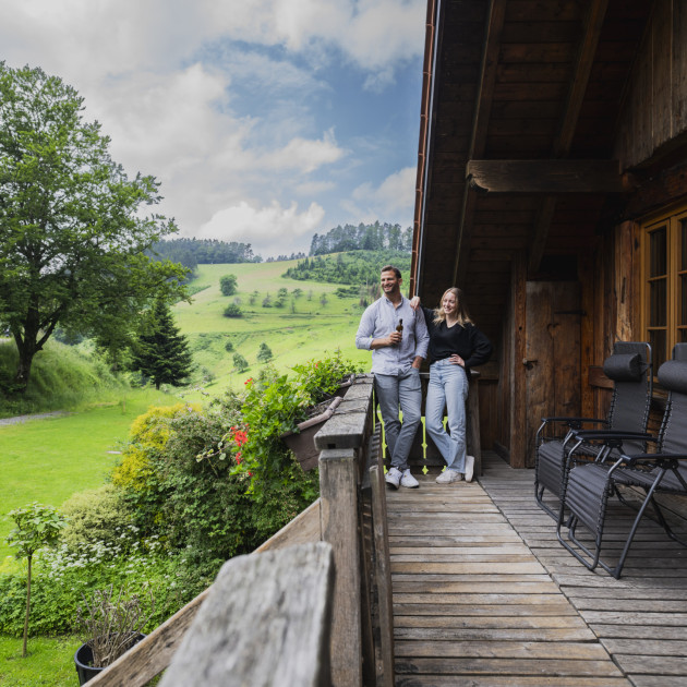 Ein junges Urlaubspaar genießt den Blick in die umliegenden Wiesen und Felder.  Zu sehen ist der Blick auf die umliegenden Schwarzwaldberge.