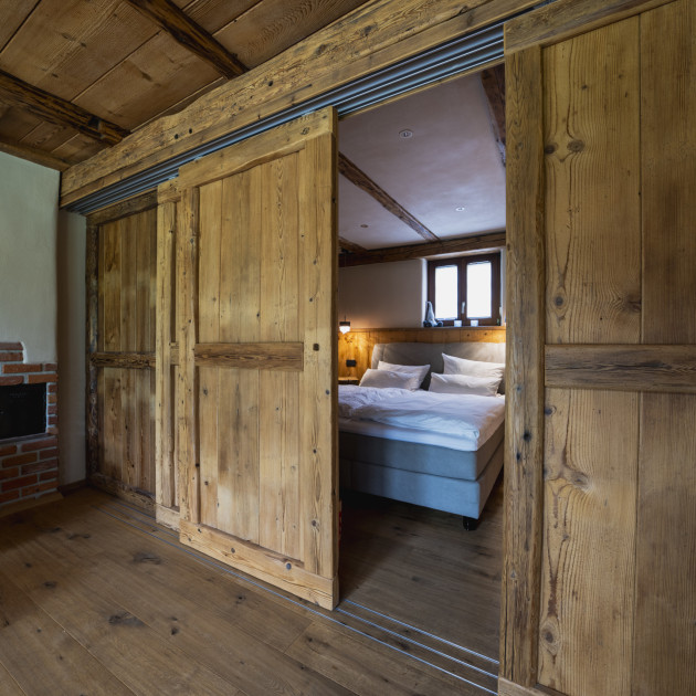Blick in den Schlafbereich der Ferienwohnung Alte Backstube. Hinter der rustikalen Holz-Schiebetür sieht man das Boxspringbett. 